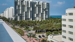 A high-rise building with multiple balconies, a parking area with cars, and a view of the ocean. - Luxury Miami Beach Apartment with Rooftop Pool (Miami Beach)