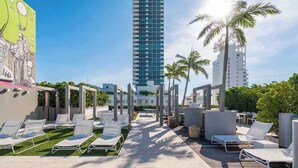 A rooftop pool area with lounge chairs, palm trees, and a tall building in the background. - Luxury Miami Beach Apartment with Rooftop Pool (Miami Beach)