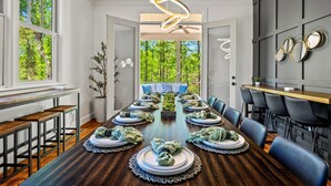Une salle à manger moderne avec une longue table en bois dressée pour un repas, entourée de chaises bleues.