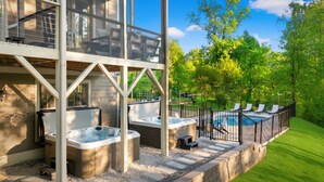 A modern outdoor hot tub area with a pool, surrounded by a wooden deck and a metal fence. - 6 King Bedrms! Heated Pool. 2 Hot Tubs. Game Room. 3 Fire Pits. Sleeps 22! (Fletcher)