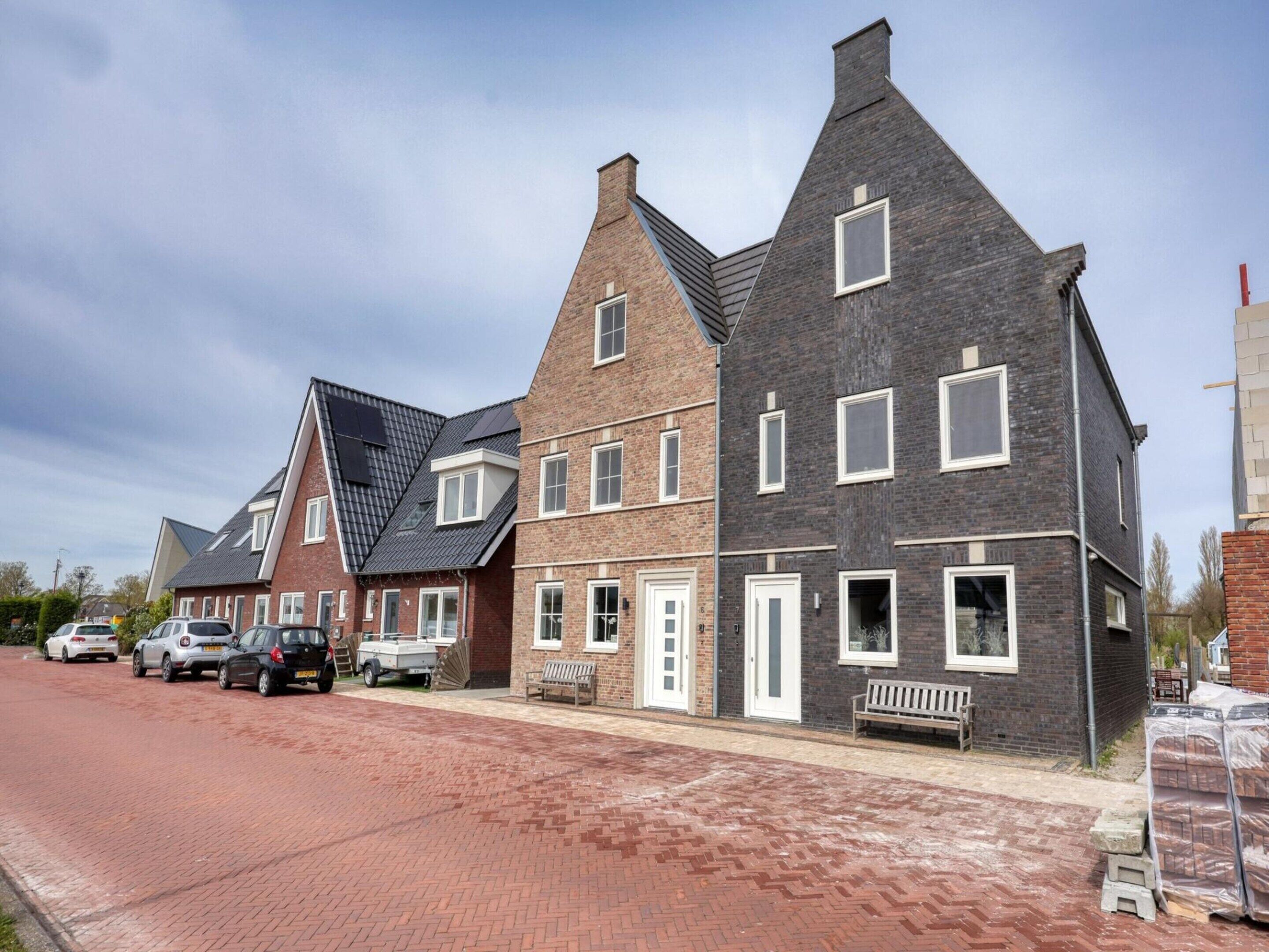A row of modern houses with brick facades and pitched roofs, a paved street, and parked cars.