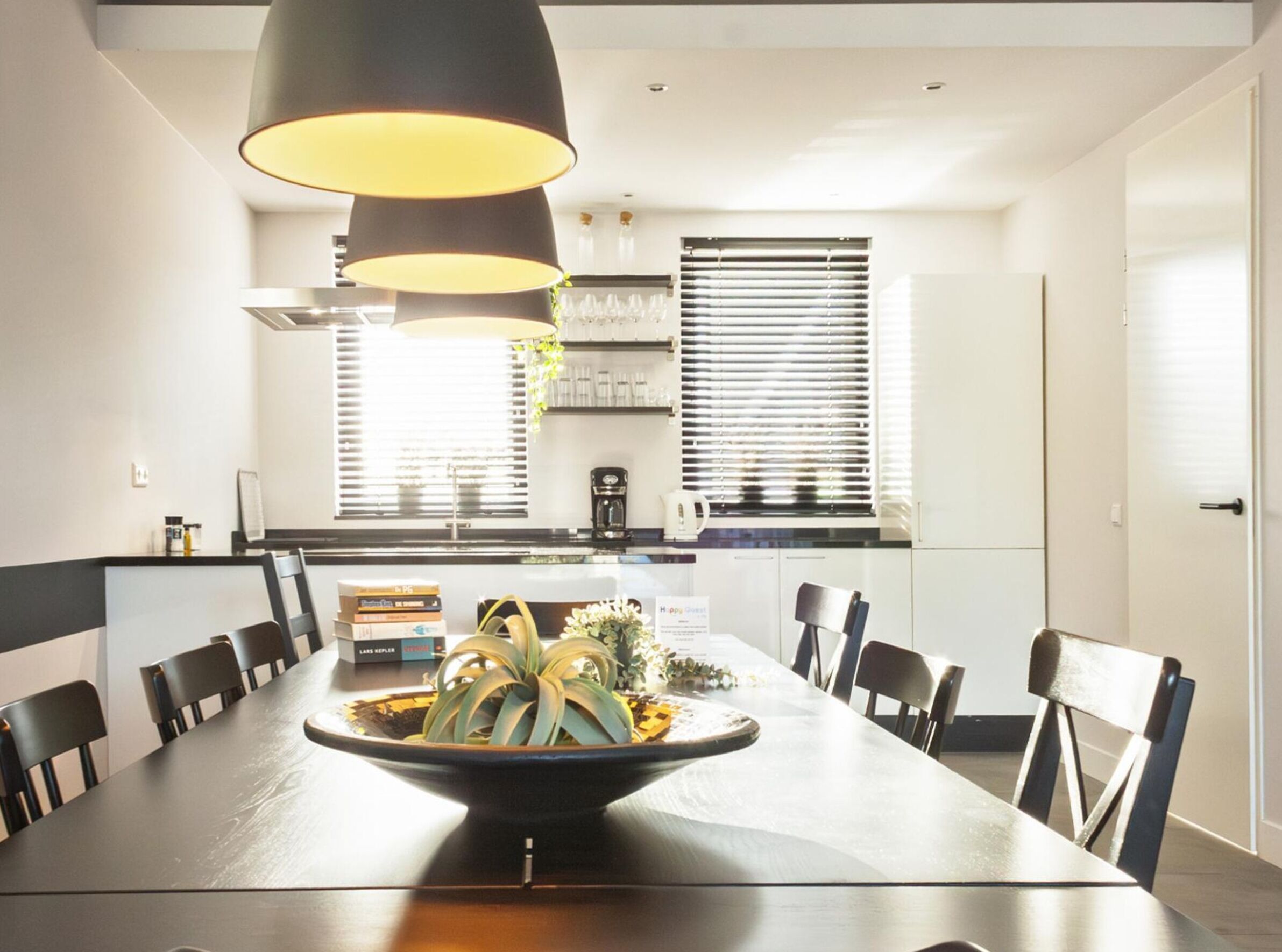 A modern dining area with a long table, black chairs, and a central decorative bowl.