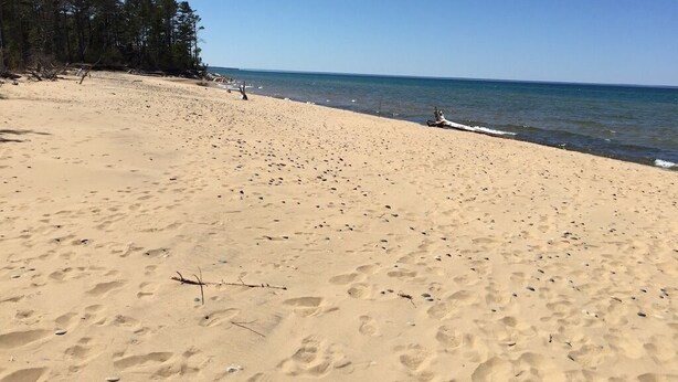 A sandy beach with footprints, a wooden structure, and a forested area. - Peaceful Couples Getaway in Lake Superior Forest (Paradise)