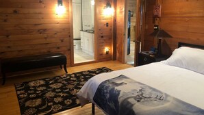 A wooden cabin room with a bed, bench, and a bathroom visible through an open door. - Peaceful Couples Getaway in Lake Superior Forest (Paradise)