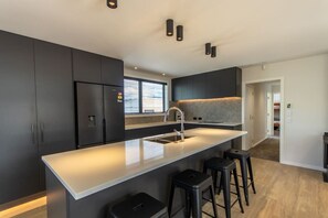 A modern kitchen with dark cabinetry, a white countertop, a stainless steel sink, and bar stools. - Maddie's Retreat, Twizel (Twizel)