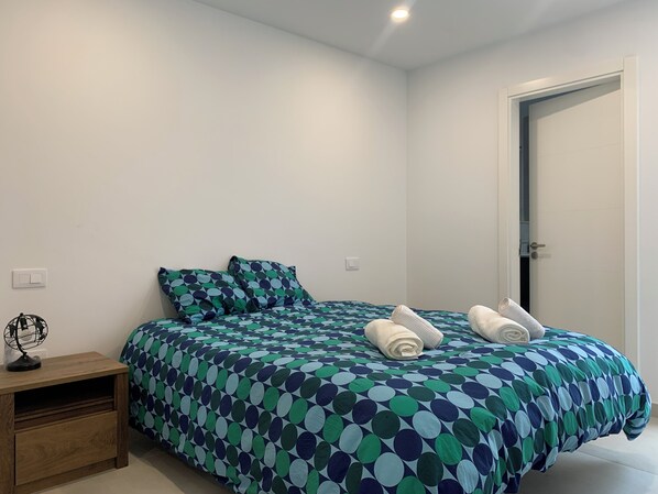 A bedroom with a bed, pillows, a nightstand, and a door.