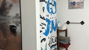 Un baño con cortina de ducha, soporte para papel higiénico, toallero, un cuadro enmarcado y una pequeña repisa con toallas.