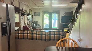 Un espacio habitable compacto con kitchenette, un sofá, una mesa de comedor y una escalera que sube a un nivel superior.
