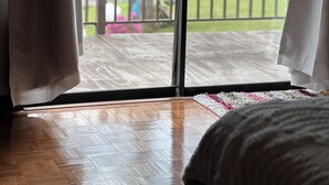 Una habitación con piso de madera, una cama y vistas a un balcón con barandilla.