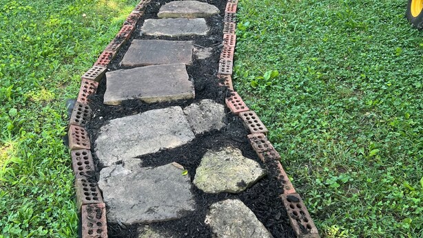 Un sendero de piedra que lleva a un edificio de ladrillo con una puerta y ventanas.