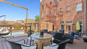 A rooftop patio with wicker furniture, a glass table, and a brick building with a fire escape. - The Arlington Apartment (Eastland)