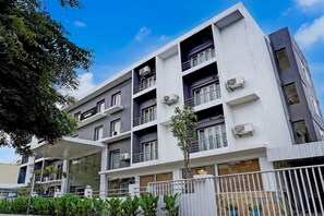 Un edificio residencial de varios pisos con balcones, unidades de aire acondicionado y un acceso con portón.