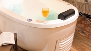 A white hot tub with a glass of orange juice, a book, and a decorative wall with a geometric pattern. - Pousada Estação Bananeiras (Bananeiras)