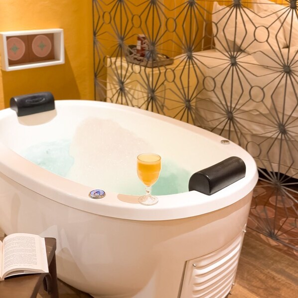 Un bain à remous blanc, un verre de jus d’orange, un livre et un mur décoratif orné d’un motif géométrique.