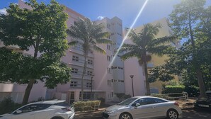 A multi-story building with a pink facade, parked cars, and palm trees. - Perla do Oceano – Funchal Sea View with XL Terrace (Funchal)