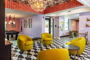 A room with a pool table, yellow chairs, a chandelier, and a patterned floor. - Hive House, Unscripted By Hyatt (Cary)