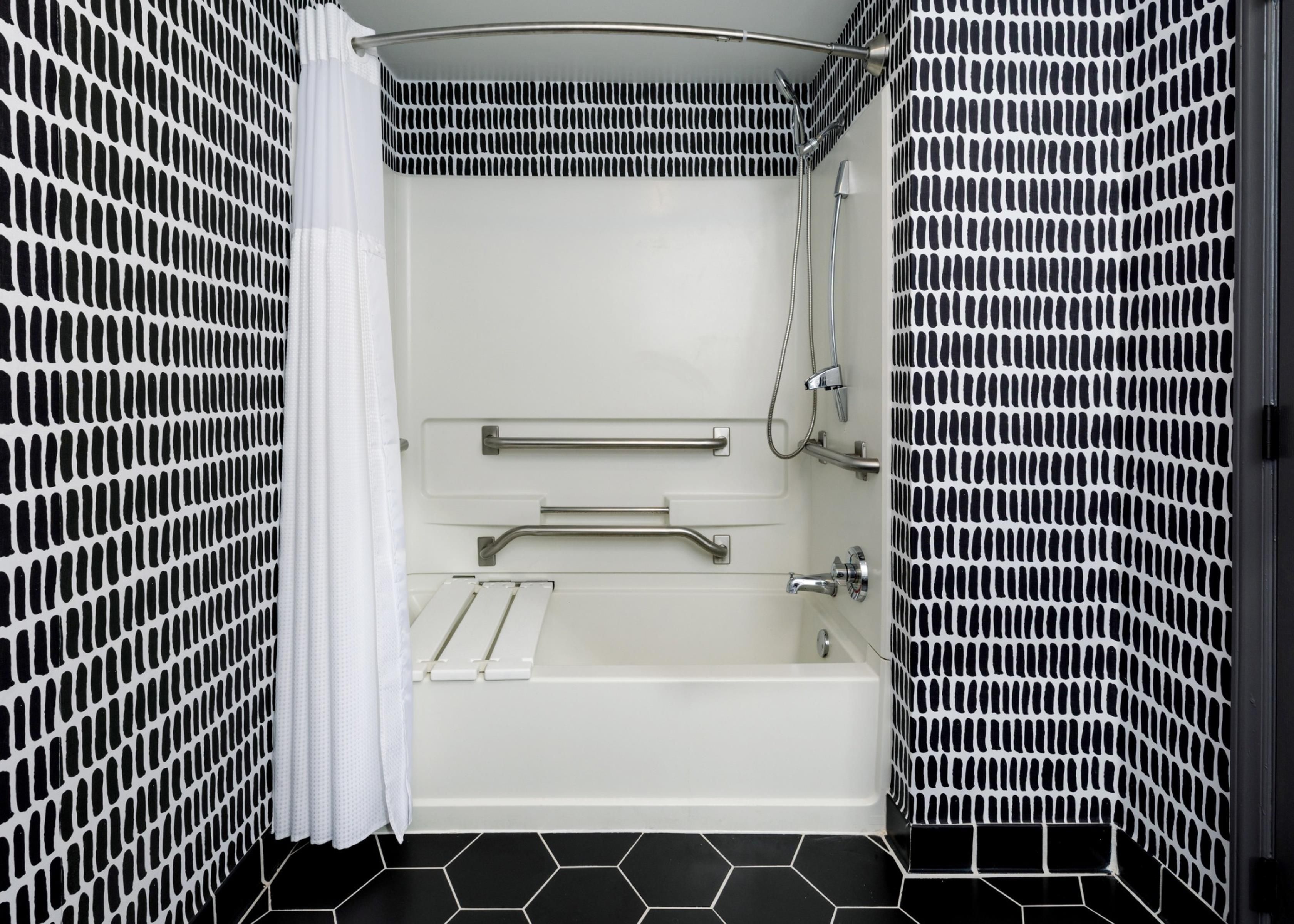 A modern bathroom with a bathtub, shower, and handrails.