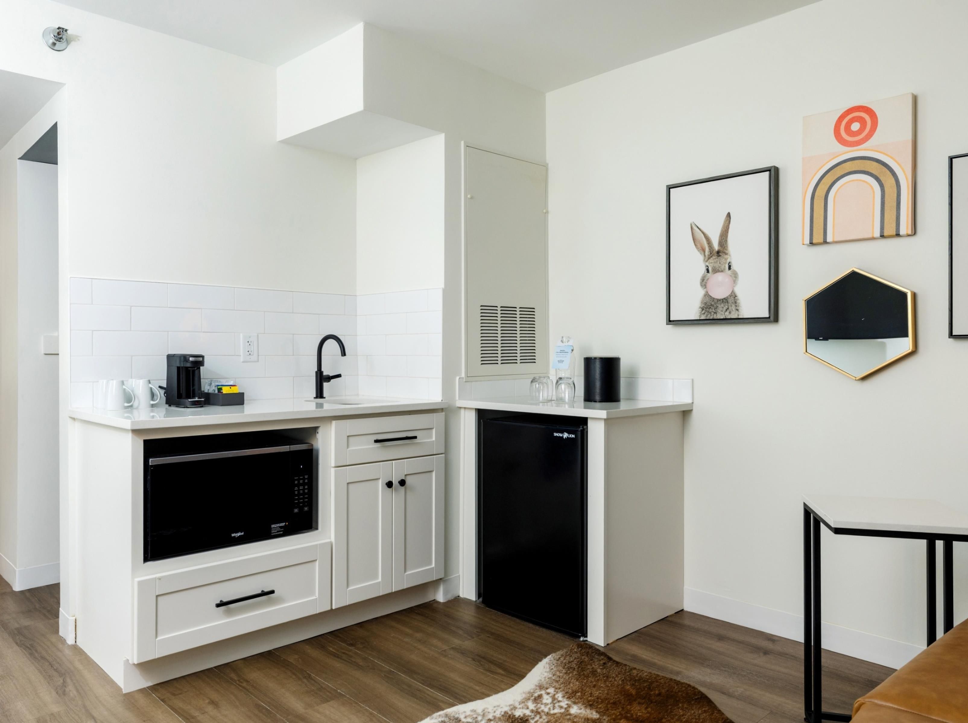 A modern kitchen with white cabinetry, a built-in oven, and a dishwasher. There are framed artworks on the wall and a small rug on the floor.
