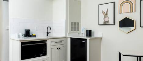 A modern kitchen with white cabinetry, a built-in oven, and a dishwasher. There are framed artworks on the wall and a small rug on the floor.