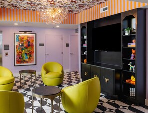 Un vestíbulo con piso de patrón blanco y negro, sillones amarillos, un mueble de entretenimiento negro y un cuadro abstracto colorido en la pared.