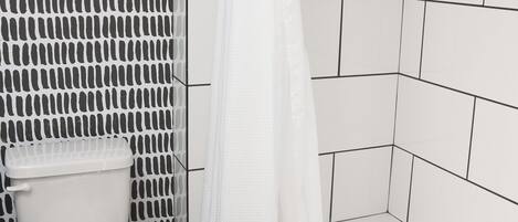 Un baño con inodoro, ducha con cortina blanca y bañera.