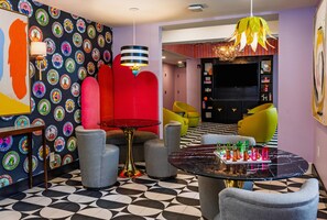 A modern living room with a black and white patterned floor, colorful wall art, and a variety of seating options including a red sofa and yellow chairs. - Hive House, Unscripted By Hyatt (Cary)