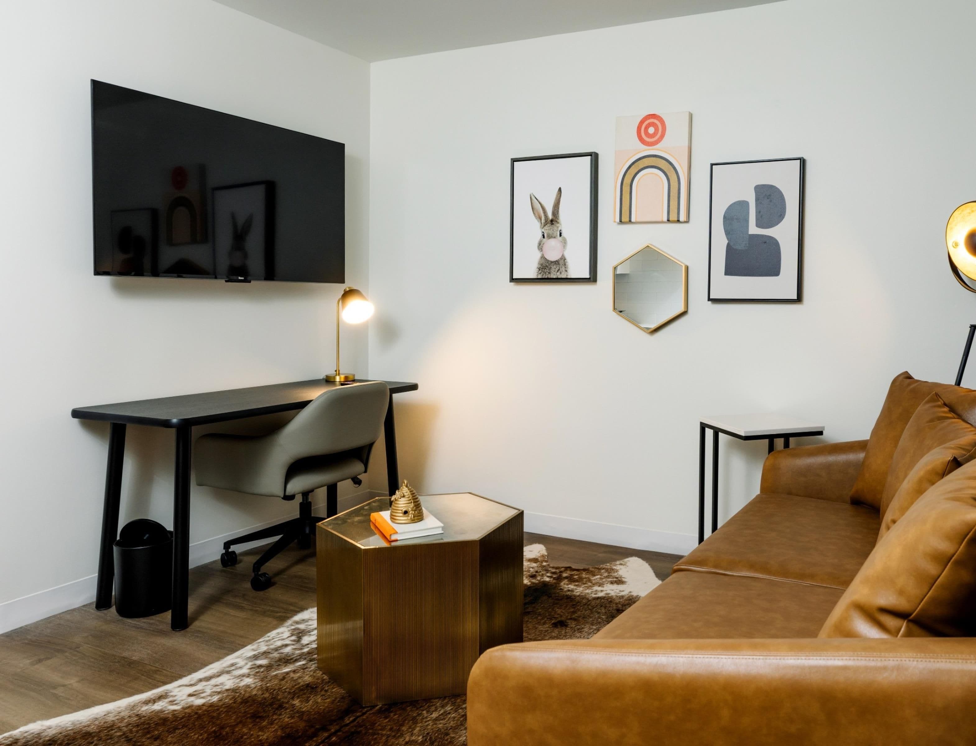 A modern living room with a leather sofa, a desk with a chair, a small side table, and wall-mounted artwork.