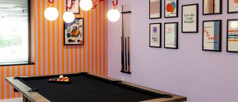 A pool table in a room with striped walls and framed artwork.