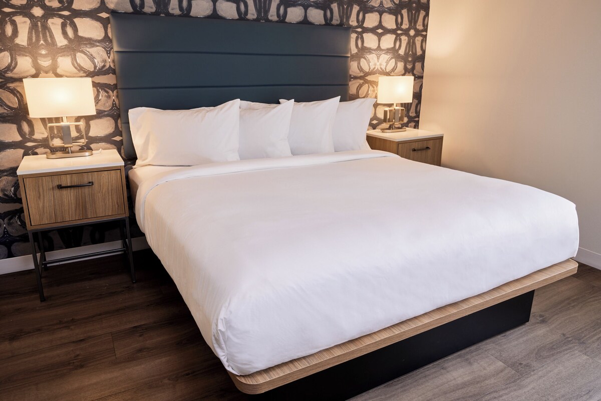 A neatly made bed with white linens, a dark headboard, and two bedside lamps on wooden nightstands.