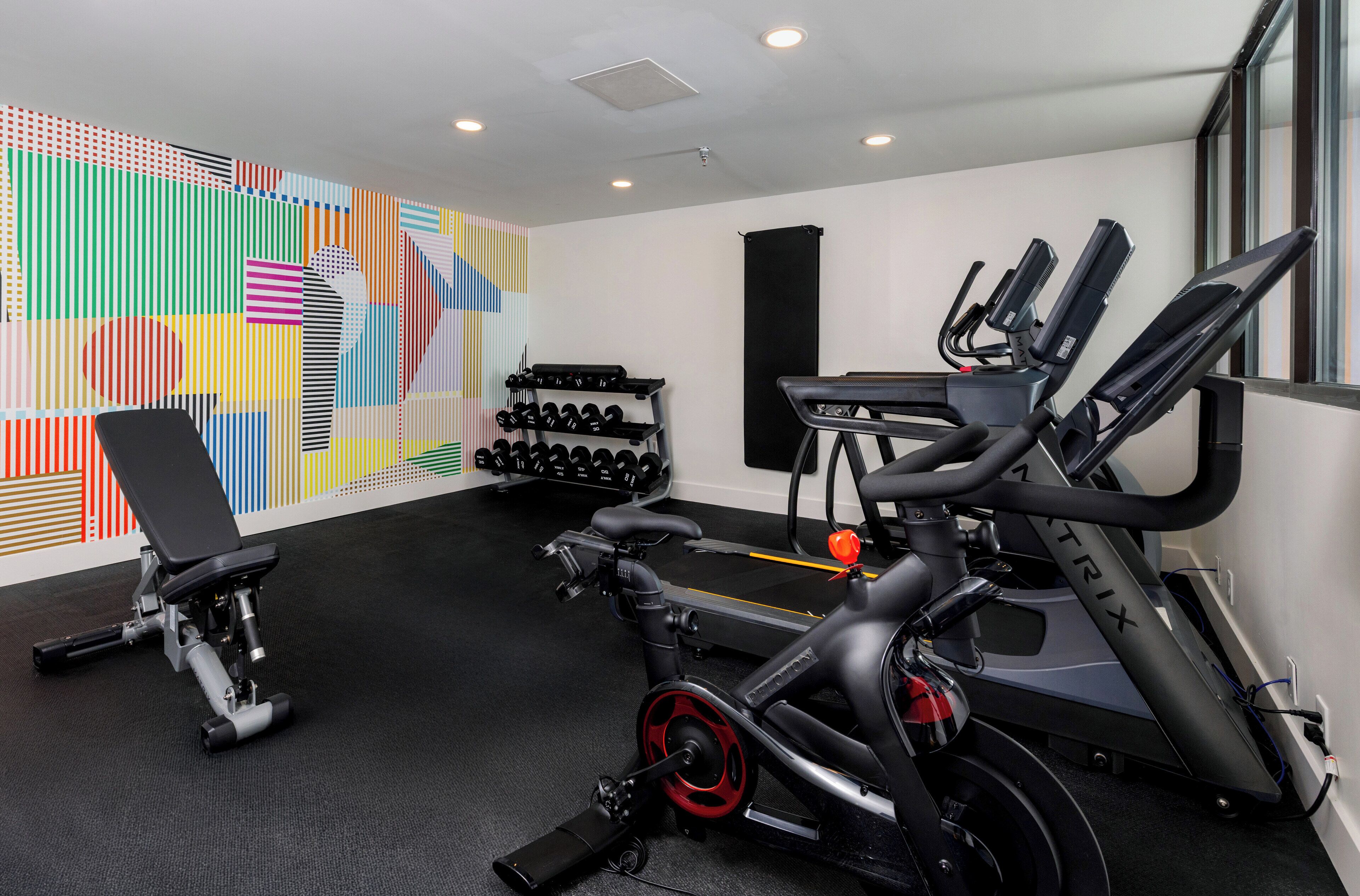 A gym with exercise equipment, a bench, and a wall with colorful geometric patterns.