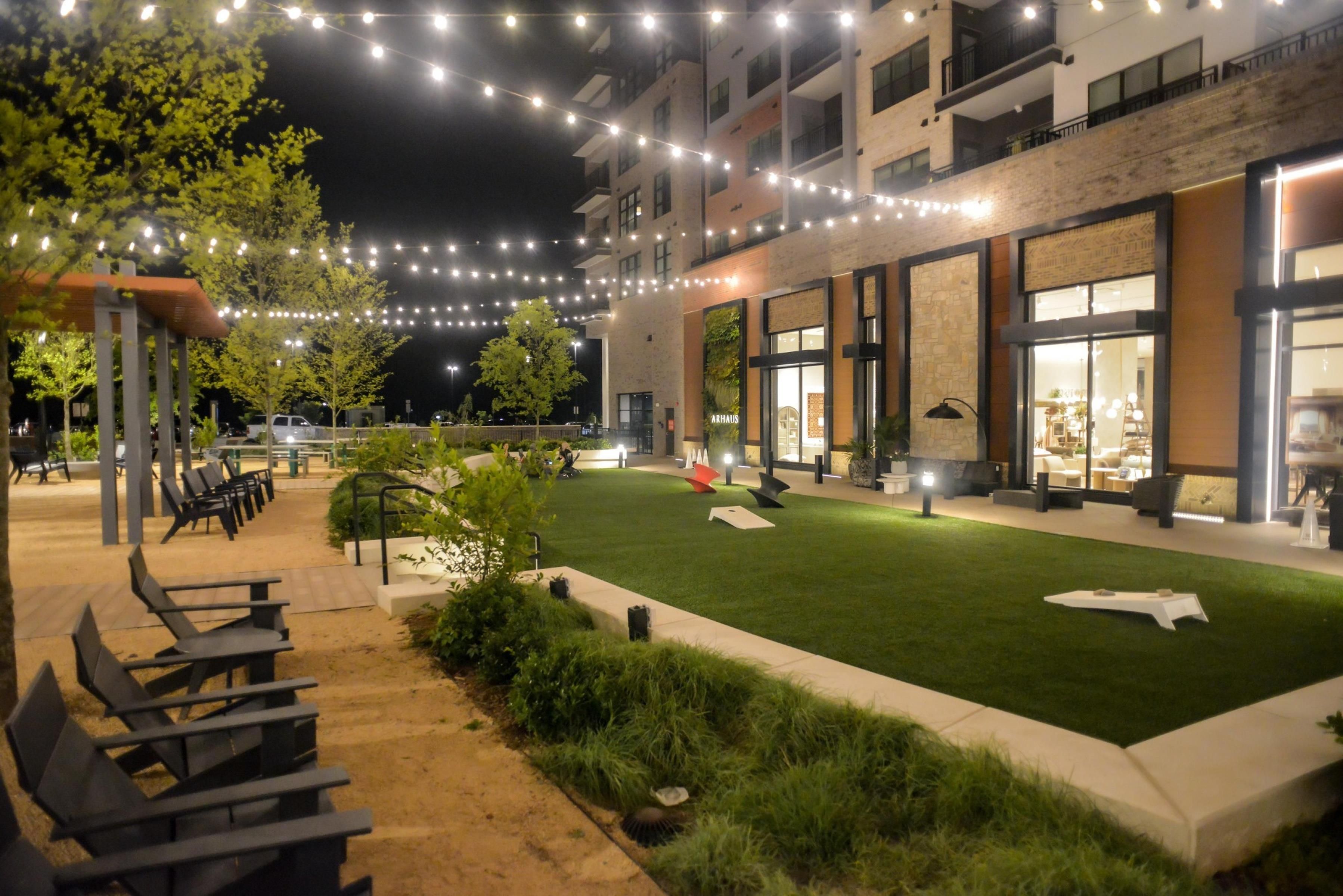 Un espacio al aire libre con césped, mobiliario y luces colgantes.