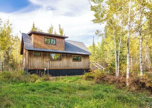 A wooden cabin with a sloped roof, surrounded by trees and grass.