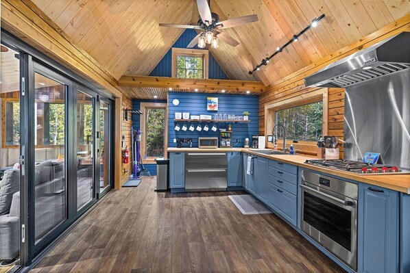 A modern kitchen with a central island, stainless steel appliances, and a wooden ceiling.