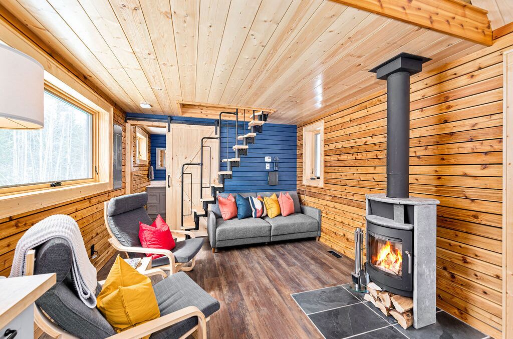 A cozy cabin interior with a fireplace, wooden walls, a sofa, and a staircase.