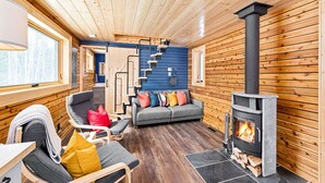 Interior acogedor de una cabaña con chimenea, paredes de madera, un sofá y una escalera.