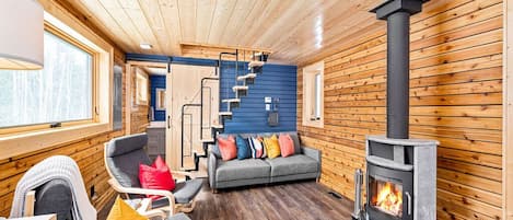 A cozy cabin interior with a fireplace, wooden walls, a sofa, and a staircase.