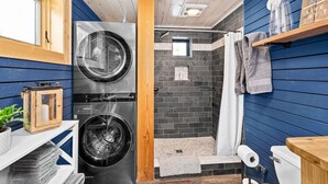 Un lavadero pequeño con lavadora y secadora, una zona de ducha compacta y un estante con toallas.