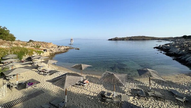 A beach with umbrellas, lounge chairs, and a lighthouse in the distance.