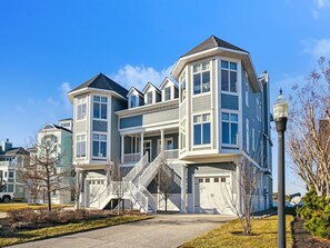 A multi-story residential building with a prominent front staircase, a garage, and a well-maintained lawn. - Bayfront Retreat | Sleeps 16 | Pool + Beach Access (Bethany Beach)
