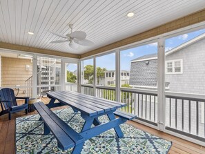 A covered patio with a wooden table and chairs, a ceiling fan, and a view of neighboring houses. - Coastal Escape w/ Views | Steps from Bethany Beach (Bethany Beach)