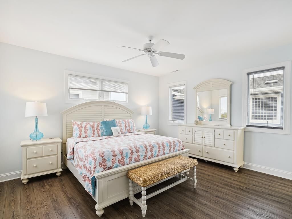 A bedroom with a bed, nightstands, a bench, a ceiling fan, a dresser, and a mirror.
