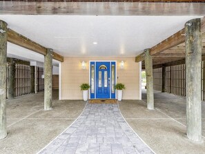 Entrada de hotel con una puerta azul, dos plantas en macetas y un camino empedrado que lleva a la puerta.