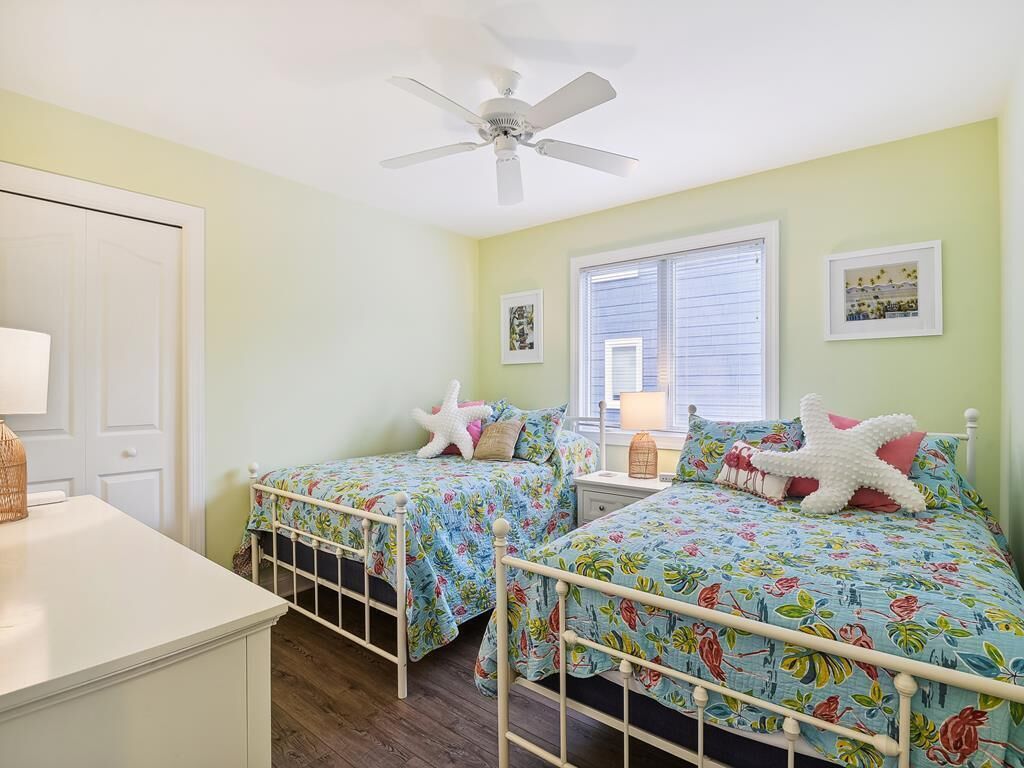 A bedroom with two beds, a ceiling fan, a window with blinds, and a door.