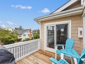 A wooden deck with a white railing, a sliding glass door, and two blue chairs. - Coastal Escape w/ Views | Steps from Bethany Beach (Bethany Beach)