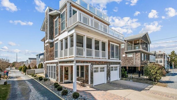 A two-story residential building with a balcony, large windows, and a garage. - Steps to Bethany Beach | Luxury Ocean Block Home (Bethany Beach)