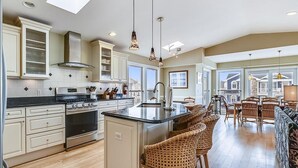 A spacious kitchen with a large island, wooden bar stools, and a dining area with wicker chairs. - Steps to Bethany Beach | Luxury Ocean Block Home (Bethany Beach)