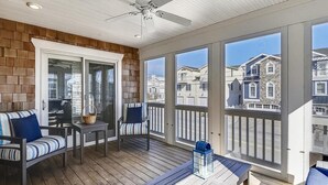 A covered patio with wooden flooring, a ceiling fan, and large windows offering views of neighboring houses. - Steps to Bethany Beach | Luxury Ocean Block Home (Bethany Beach)