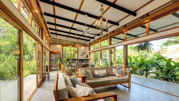 A spacious living area with large windows, a sofa set, and a dining table. - Villa Opalo (Cahuita)