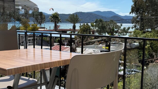 A balcony with a wooden table and chairs, overlooking a lake with mountains in the background. - Elitaş Apart Otel (Fethiye)