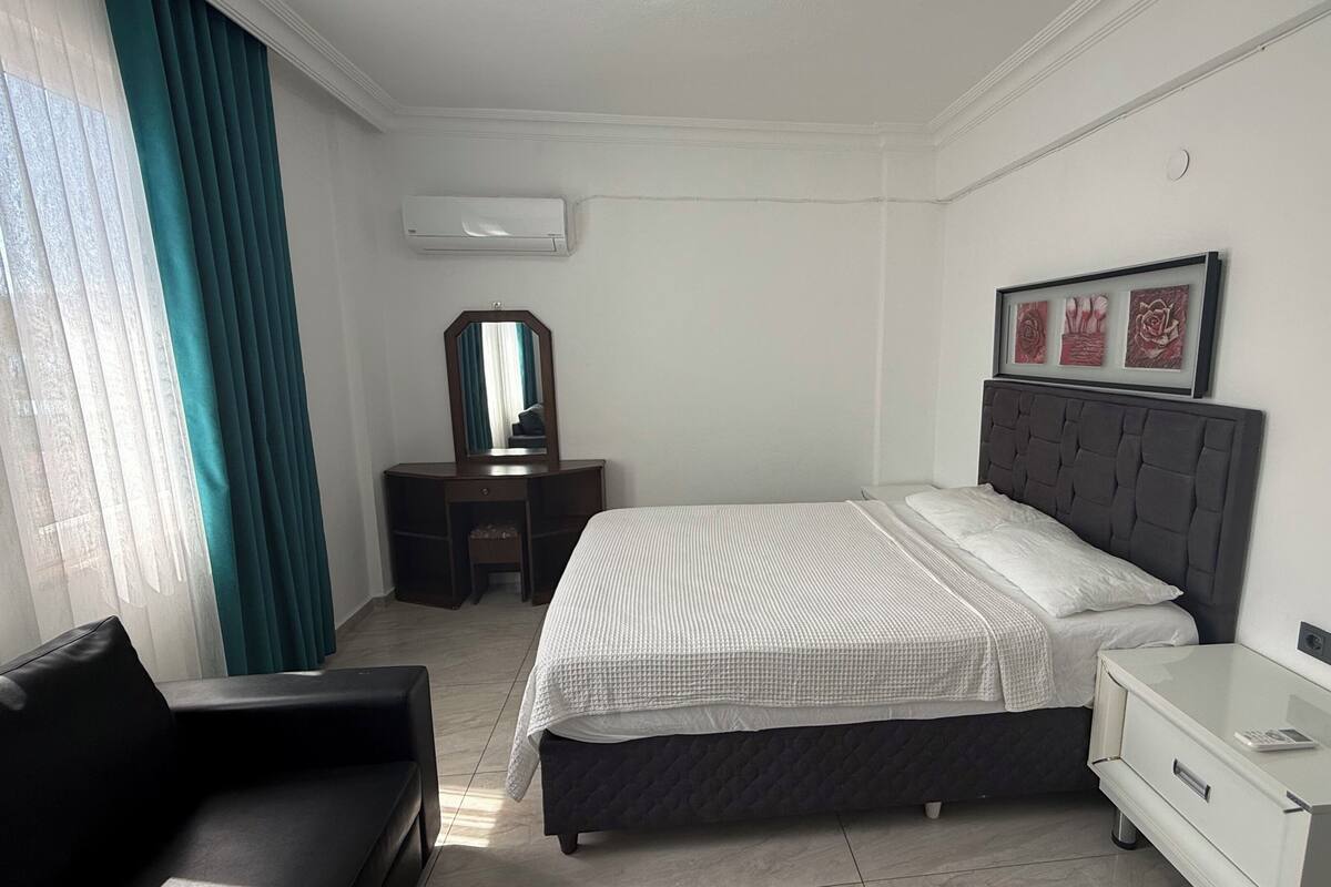 A hotel room with a bed, a desk, a chair, a dresser, a mirror, and a framed picture on the wall.